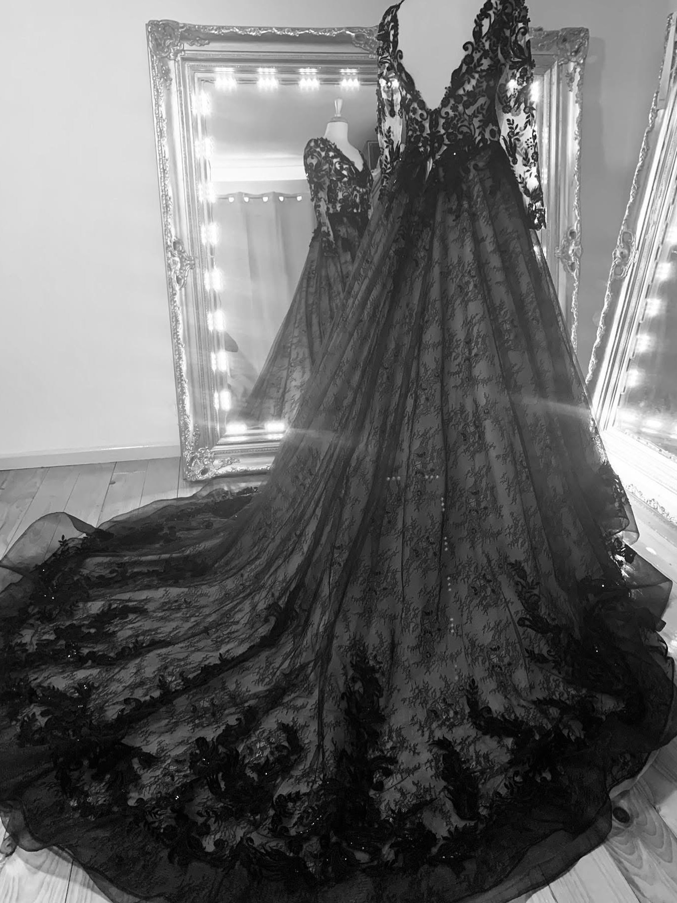Maggie Sottero black lace wedding gown with nude underlay, long sleeves and cathedral train displayed on a mannequin in front of an ornate lit mirror — bridal alterations by Jacqui