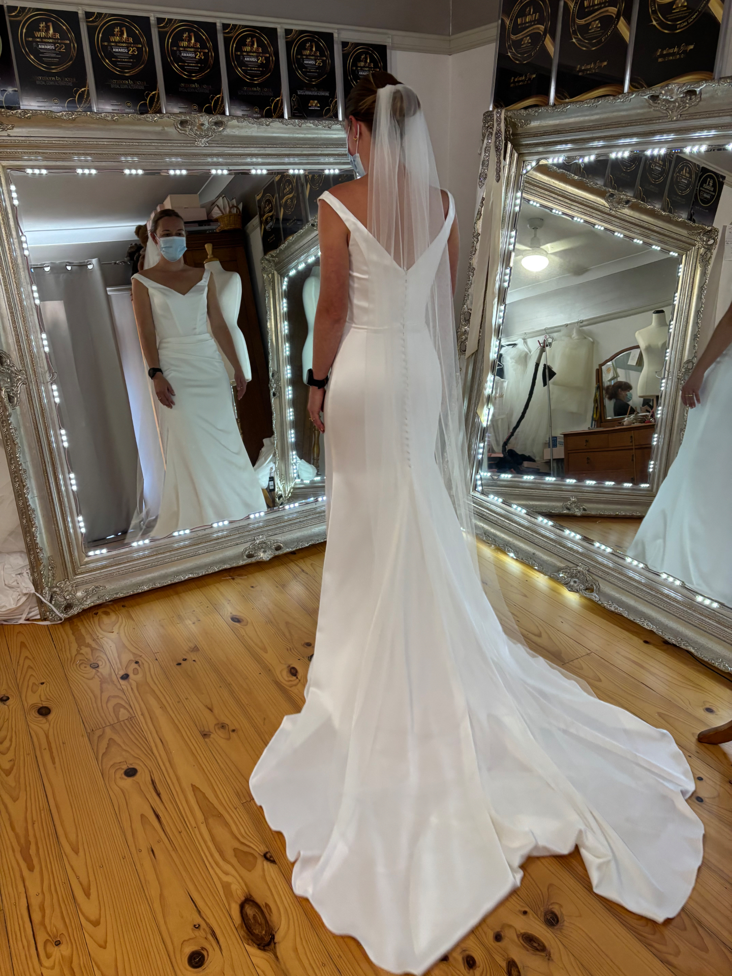 Bride from behind in a fitted crepe V-back wedding gown with covered button train and cathedral veil after wedding dress alterations by Jacqui