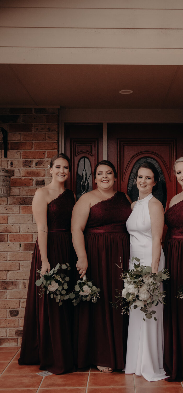 Bridesmaids in burgundy one-shoulder gowns after bridal party alterations by Jacqui