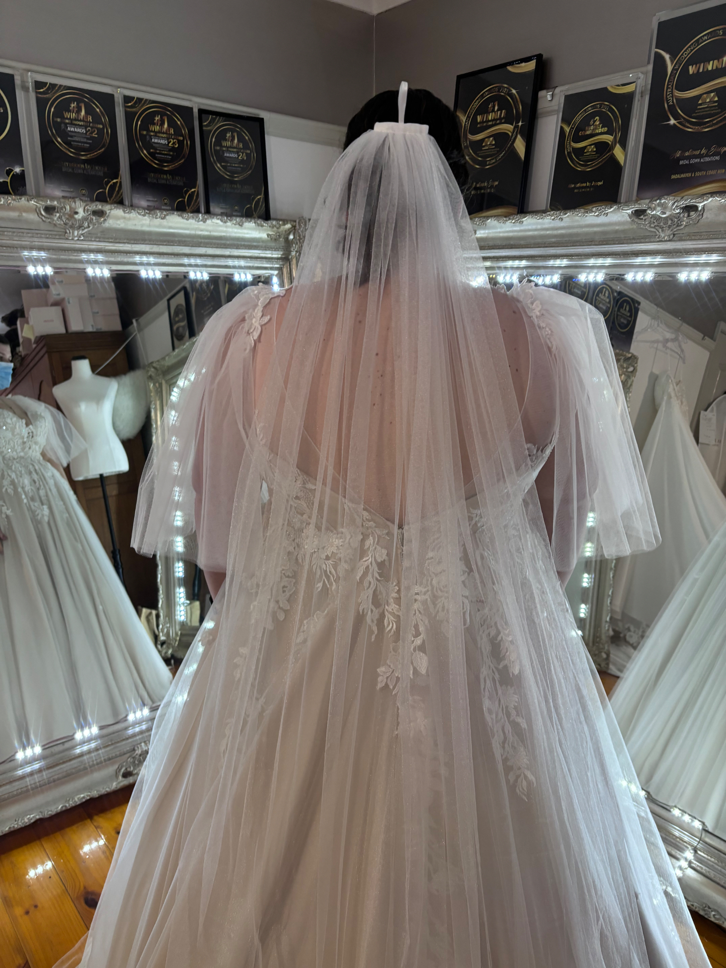 Bride from behind in a blush tulle A-line gown with floral lace appliqué, soft cathedral veil and hand crafted custom tulle sleeves — alterations by Jacqui to complete the bride's vision