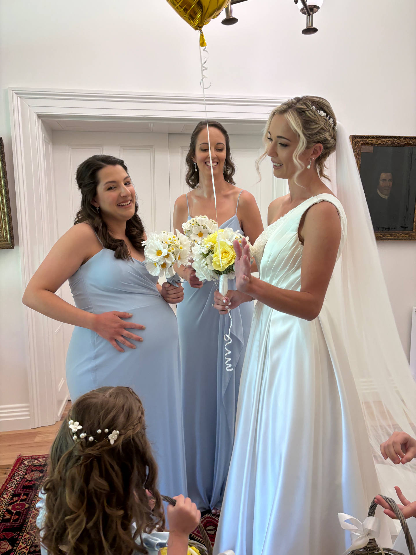 Bride in an ivory satin gown with long veil standing beside bridesmaids in powder blue dresses holding bouquets indoors — bridesmaid dress alterations and resizing by Jacqui