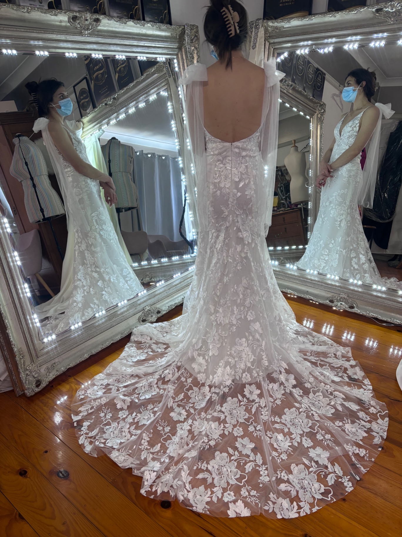 Bride from behind wearing a fitted floral lace wedding gown with tulle shoulder bows and long lace train — train alterations and lace applique work by Jacqui