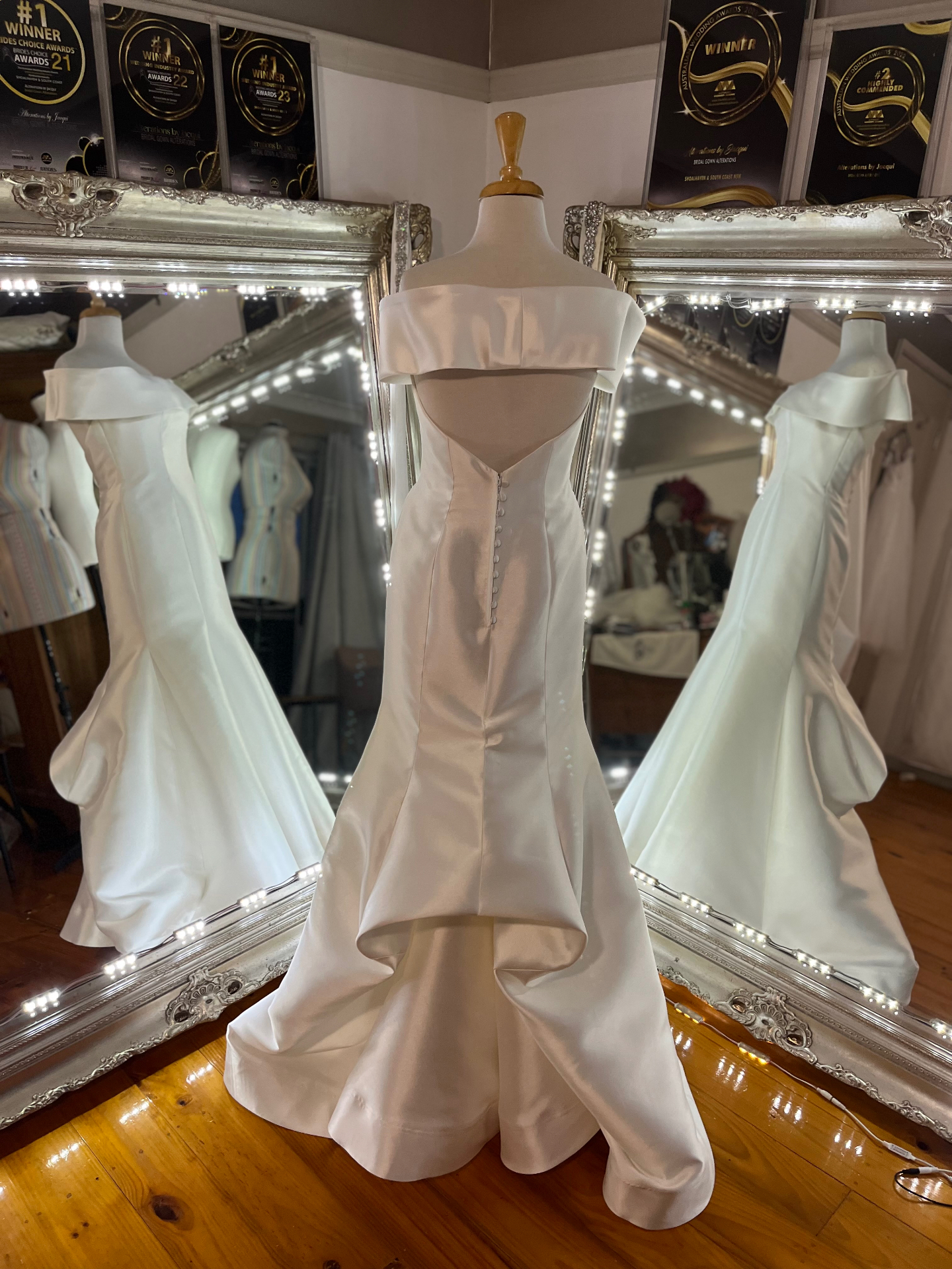 Ivory silk off-shoulder mermaid wedding gown with covered button back on a mannequin — resizing, hemming, steamed and hand crafted bustle by Jacqui