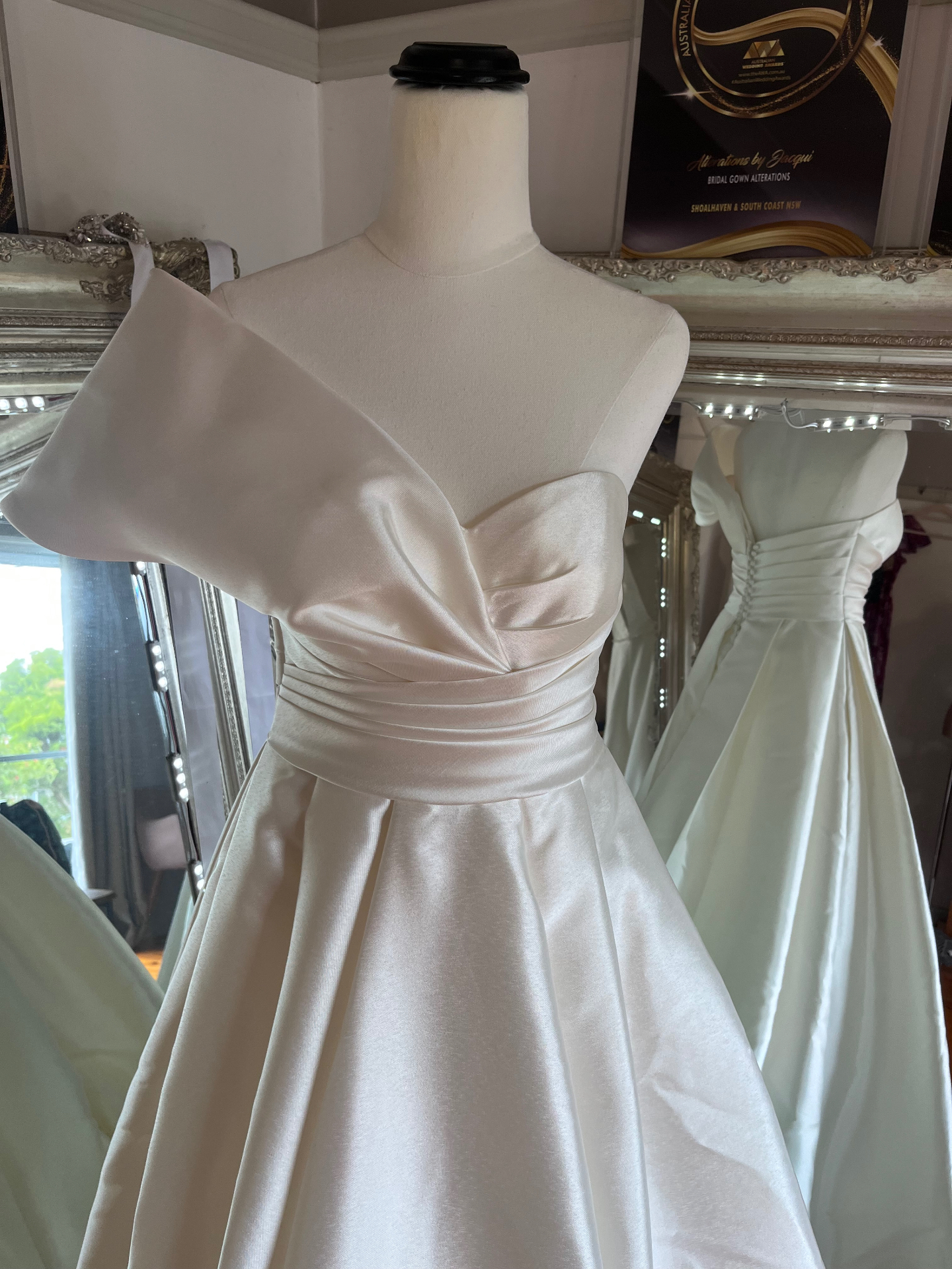 Ivory satin wedding gown with asymmetric one-shoulder draped bodice and full pleated skirt on a mannequin — steaming, alterations and hoop hire by Jacqui