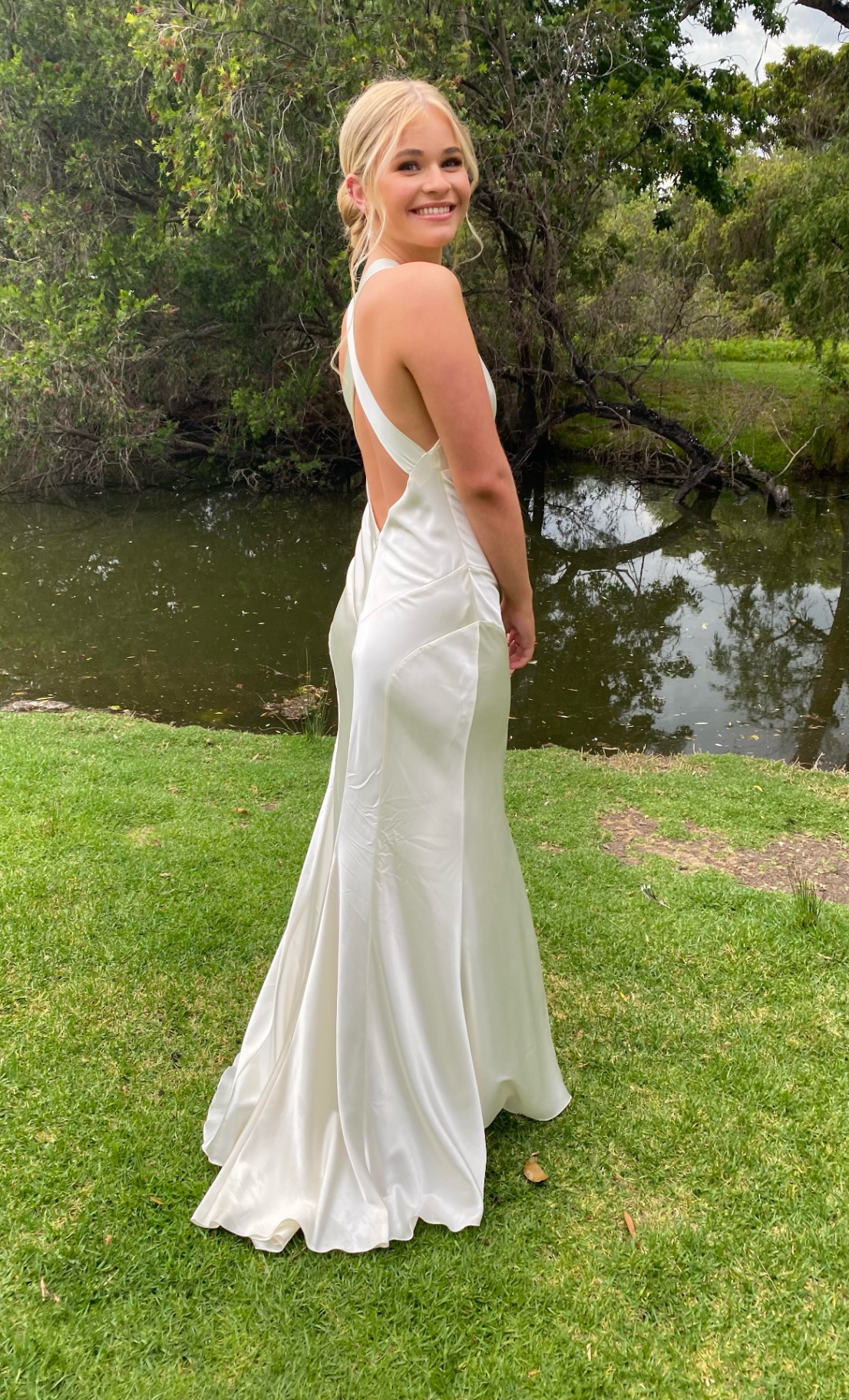 Young woman in an ivory silk bias-cut formal gown with open cross-back, photographed beside a pond — formal dress alterations and resizing by Jacqui